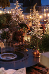 Outdoor winter terrace with vintage suitcases, snow-covered pine trees, fairy lights, rustic wooden elements, and holiday decor