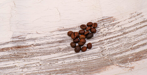 A small pile of dark roasted coffee beans sits on a textured ground. Providing an empty area and a rustic layer for potential writing space. Excellent for cafe branding.