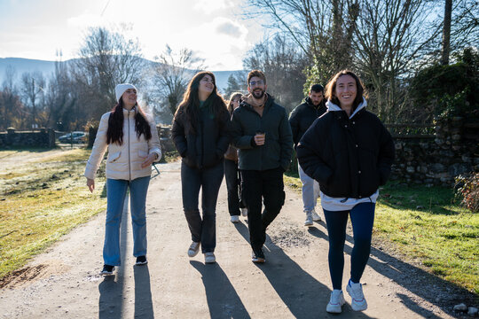 Group of young friends walking and laughing on a country road, enjoying leisure time and friendship in nature
