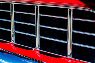Close-up  of a red vintage truck's grille and bumper reflecting off their chrome.