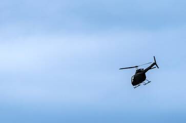 Single helicopter flying at an angle silhouetted against a pale blue sky