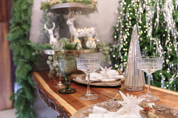Christmas table decorated with elegant plates, deer figurines, glassware and festive tree with sparkling lights