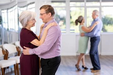 Fototapeta premium Middle-aged man paired senior woman and leisurely dancing slow dance in studio for beginners learning pair dancing. Woman clung to her partner, put her head on mans shoulder