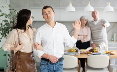 Fototapeta premium Grumpy elderly parents condemn and look unkindly after newlyweds. Family conflict, pensioners send their son with girlfriend out of apartment. Dispute discord within family, condemnation and rejection
