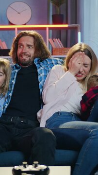 Likable frightened excited parents and their two kids previsioning scary movie on TV set in the evening at home they screaming from scare and closed their eyes