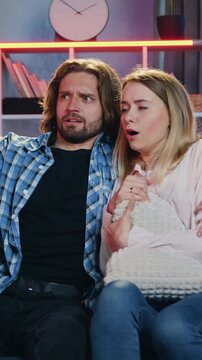 Family leisure concept where likable scared parents sitting with embraces on the couch in sitting room during previsioning scary movie on TV set while their son and daughter hidding out near the couch