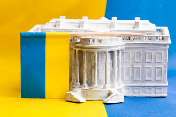 A figurine of the White House against the backdrop of the Ukrainian flag. Concepts of US aid to...