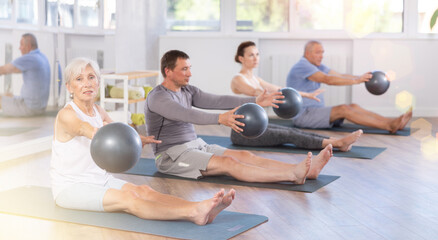 Elderly woman exercising pilates with soft ball in group in fitness studio