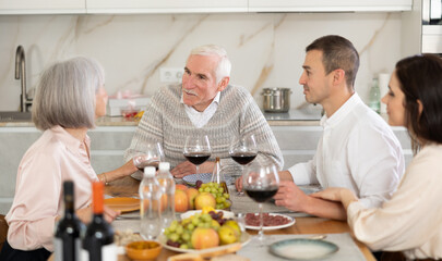 Happy senior parents and young couple talking while drinking wine sitting around kitchen table