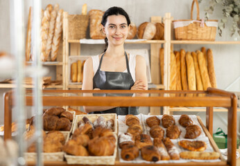 Armenian adolescent girl work sell in family bakery shop. She sells bakery products, stand near window and greet visitors. Entrepreneurs present goods in showcase, demonstrate sweet pastries
