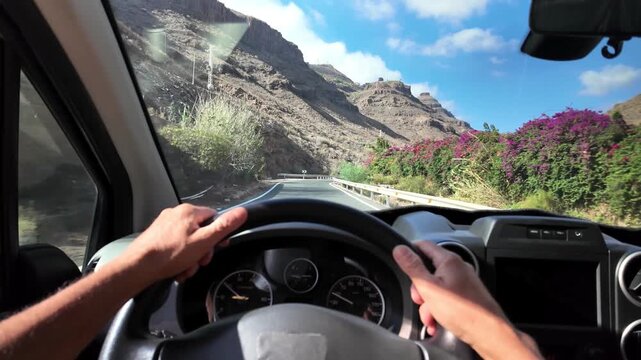 Driver's point of view driving a minivan on a curvy road through the arid volcanic canyons of Gran Canaria, on a sunny day during a vacation road trip on the island of Spain