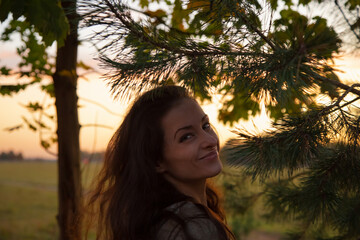 Beautiful woman in a park touching hand and looking on a Christmas green tree with happy smiling in sunset sky light on the street outdoor with copy space nature beautiful background.