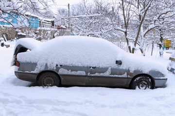 A gray car covered in thick snow in a winter landscape
