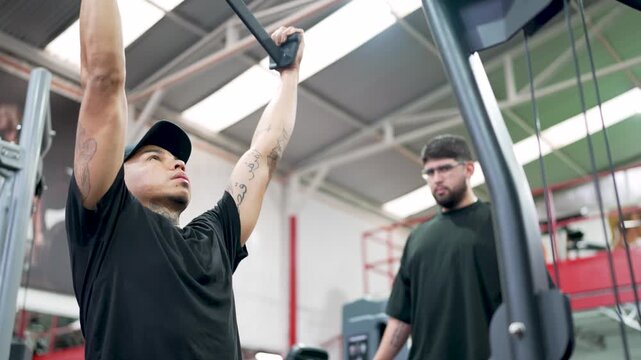 Personal trainer coaching a tattooed man doing a lat pulldown back exercise in a modern gym