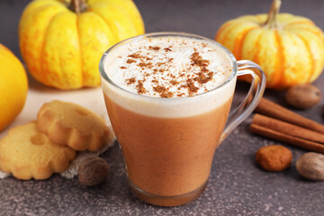 Delicious pumpkin latte in glass cup, spices, cookies and fresh vegetables on grey textured table, closeup