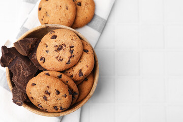 Yummy chocolate chip cookies and pieces of chocolate on white tiled table, flat lay