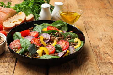 Tasty lentil salad with ingredients and bread on wooden table, closeup