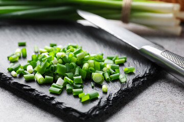 Cut green onions and knife on light grey table, closeup