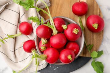 Fresh radishes with green leaves and bowl on white marble table, flat lay