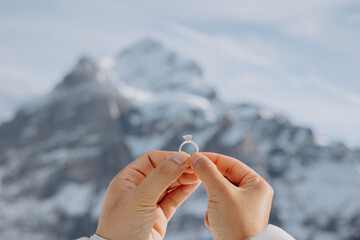 Young woman holding out her hand with an engagement ring against a mountain landscape background