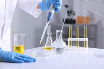 Scientist with dripping motor oil into Petri dish at table in laboratory, closeup
