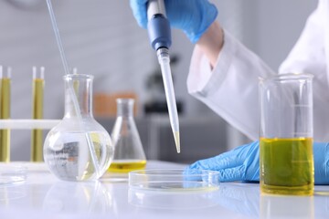 Scientist with dripping motor oil into Petri dish at table in laboratory, closeup