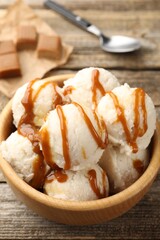Tasty ice cream with caramel sauce in bowl on wooden table, closeup