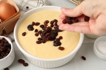 Making muffins. Woman adding raisins to dough at white table, closeup