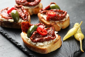 Delicious bruschettas with cream cheese, sun-dried tomatoes, chili pepper and green olives on table, closeup
