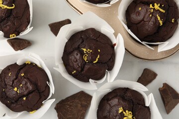 Naklejka premium Tasty chocolate muffins with lemon zest on white table, flat lay