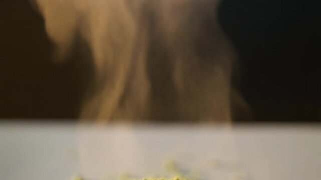 Close-up abstract of yellow particles scattering with wisps of smoke or steam rising against a dark background, highlighting a dynamic texture and movement