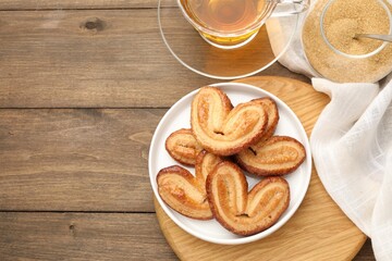 Yummy palmiers, tea and brown sugar on wooden table, flat lay. Space for text
