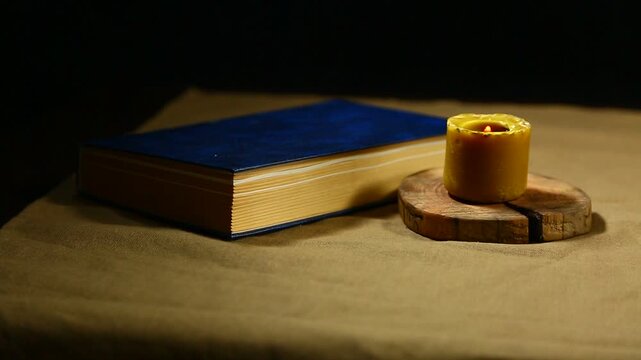 Burning wax vintage candle with blue book on the  table on dark black background with copy space. Ancient old education creative idea concept in candle light