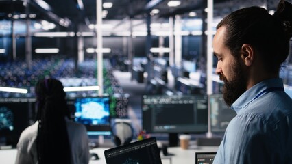 Close up of developer in data center coding with generative AI assistance on laptop. IT expert leveraging artificial intelligence large language model on notebook to solve tasks, camera A