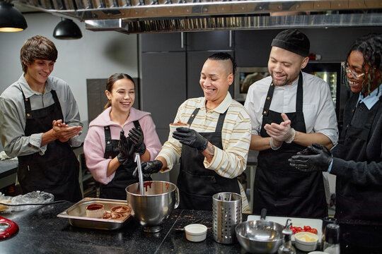 Group of young adult multiethnic men and women standing in kitchen preparing dessert together, smiling and laughing