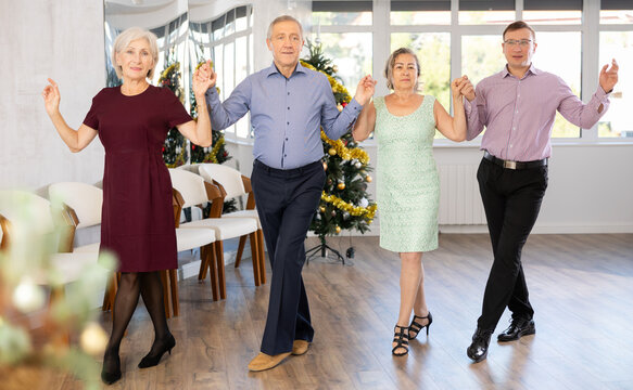 Happy adult people dancing Irish folk dance in row at modern ballroom on Christmas