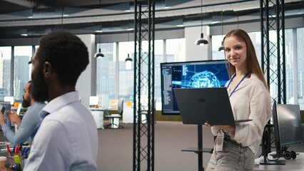 Fototapeta premium Portrait of young smiling female programmer in office automating repetitive tasks using AI scripts. Cheerful junior developer using artificial intelligence to speed up feature implementation, camera A
