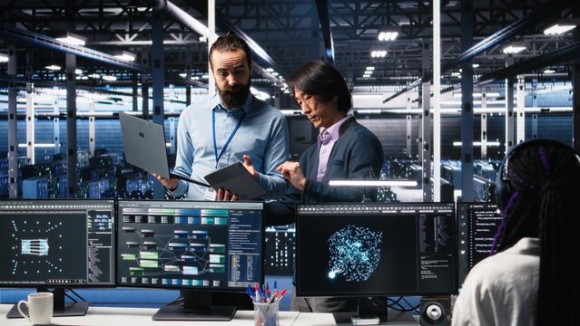 Data center manager supervising developer using device to monitor neural network AI LLMs. Team leader checking progress done by worker overseeing servers powering machine learning processes, camera A - Powered by Adobe