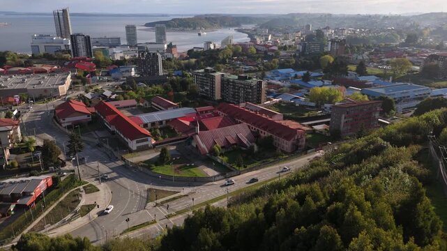 Aerial parallax view over hilltop trees revealing busy street intersection.