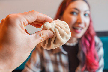 Hand holding a delicious Georgian khinkali hot dumpling, offering it to a young woman eagerly...