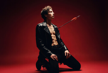 Fototapeta premium Attractive man kneeling with an arrow through his chest in a dark studio with dramatic lighting, conveying themes of vulnerability and emotional pain.
