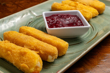 Crispy Fried Breaded Cheese Sticks with Red Dipping Sauce Served on Green Rectangular Plate over Rustic Wooden Background