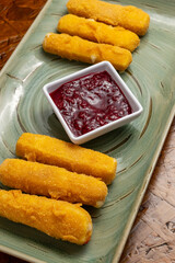 Crispy Fried Breaded Cheese Sticks with Red Dipping Sauce Served on Green Rectangular Plate over Rustic Wooden Background