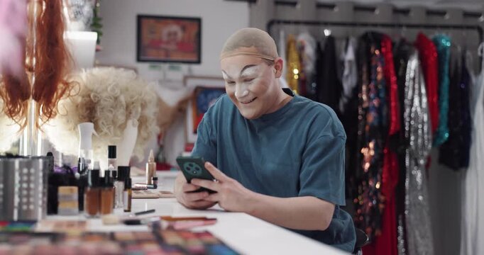 Makeup, phone and laugh with drag performer in studio for contact, alter ego transformation and lgbt culture. Cosmetics, communication and theater with person backstage for costume and joke.