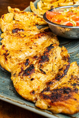 Close Up of Juicy Grilled Chicken Breast Fillet with Sear Marks Served with Fresh Salad and French Fries on Green Plate