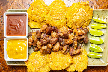 Traditional Colombian Chicharr&oacute;n with Fried Plantains, Lime and Dipping Sauces, Crispy Pork Belly Close Up