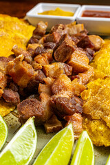 Traditional Colombian Chicharr&oacute;n with Fried Plantains, Lime and Dipping Sauces, Crispy Pork Belly Close Up