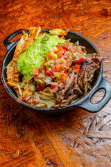 Cast Iron Skillet with Loaded Fries, Grilled Mixed Meat, Guacamole and Pico de Gallo Salsa on Wooden Background