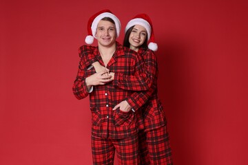 Happy couple in Santa hats and pajamas on red background. Christmas atmosphere