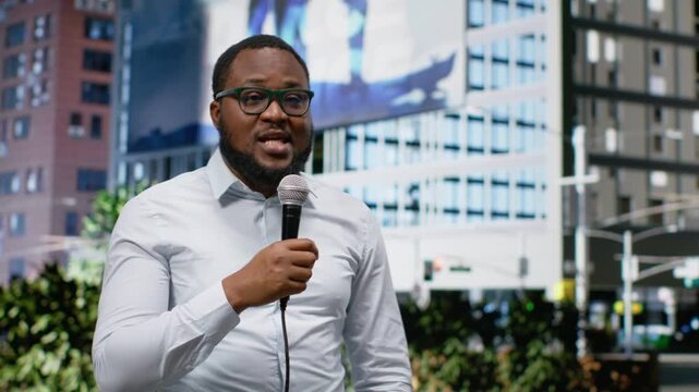 Adult male correspondent conducting public interview on city street, using confident dialogue to share news coverage. Demonstrating skill in storytelling in a metropolitan center. Camera B.